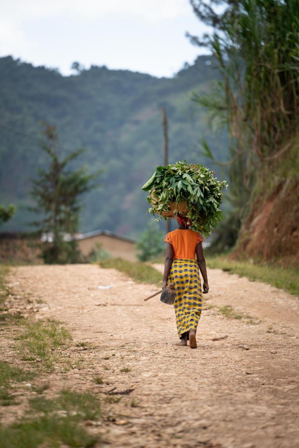 woman with basket on head walking away on dirt road