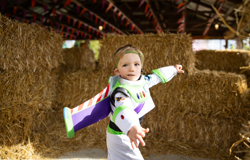 child in Toy Story costume in front of bails of hay