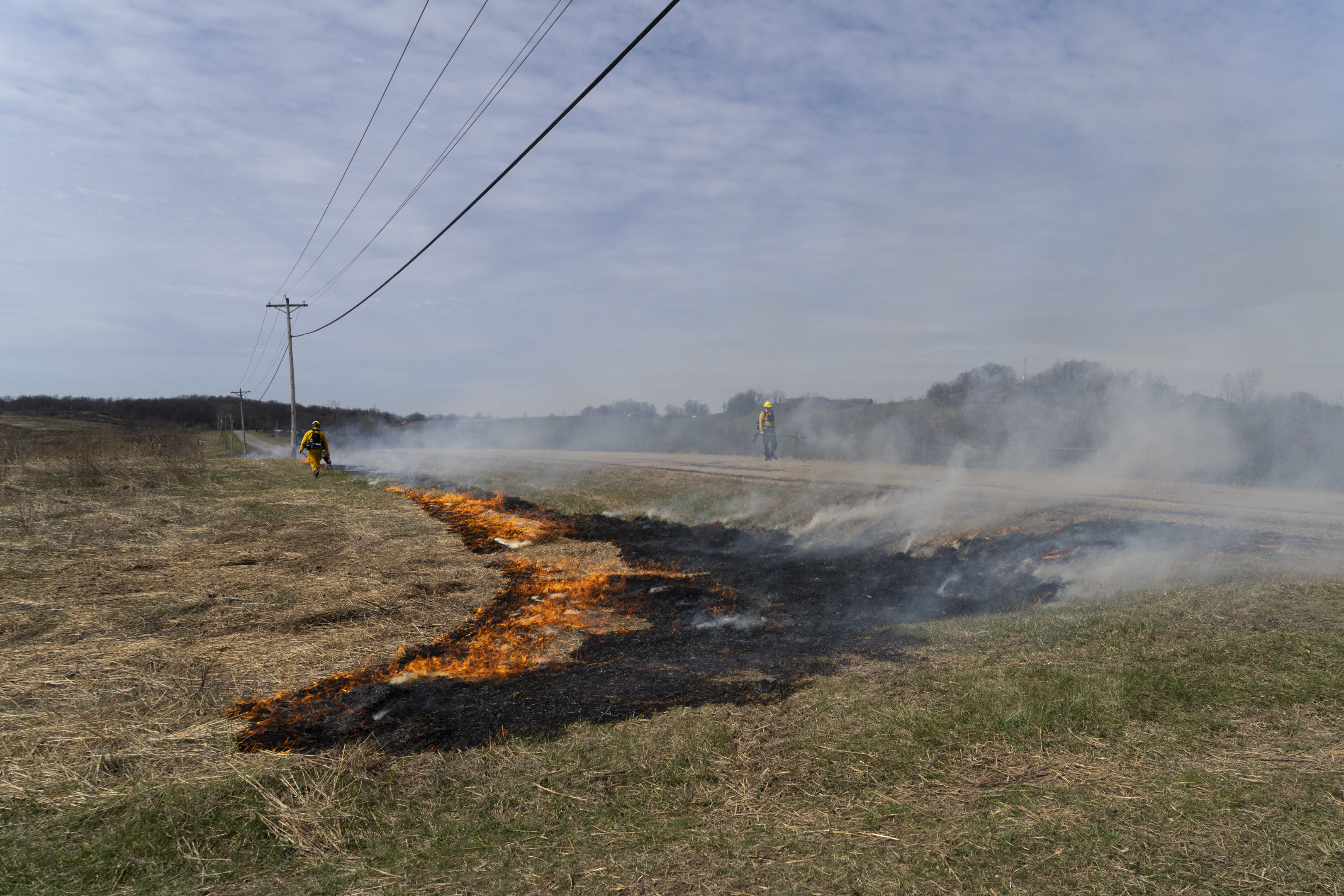 two firefighters walking on either side of a prescribed burn