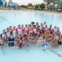 Children and lifeguards gather for group photo in pool after swim lesson