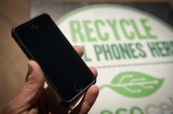 Photo showing a hand holding a phone, with a sign behind that reads "Recycle old phones here"