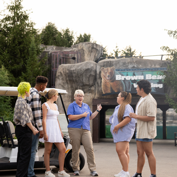 Zoo guide leading tour and pointing to bear habitat